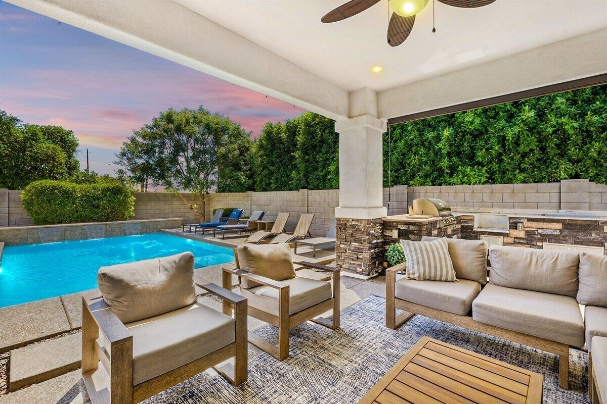 An outdoor pool area with lounge chairs, a stone fireplace, and a view of the surrounding greenery.