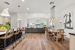 A spacious kitchen with a dining area, wooden flooring, and modern pendant lighting.