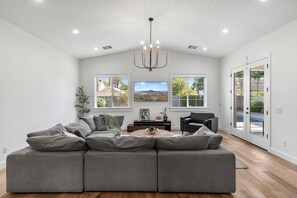 A spacious living room with a large gray sectional sofa, a round coffee table, and a chandelier.