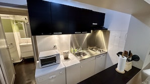 A compact kitchen with a microwave, sink, and stove, featuring modern appliances and black cabinets. - Nature Refuge Near the Trail (Mont-Dore)