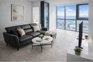 Ein modernes Wohnzimmer mit einem schwarzen Ledersofa, einem runden Couchtisch und einem großen Fenster mit Blick auf die Stadt.