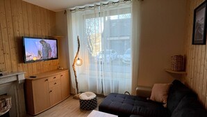 Una sala de estar acogedora con un sofá oscuro, un mueble de madera, un televisor y una lámpara.