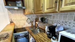 Una cocina compacta con gabinetes de madera, un lavamanos de acero inoxidable, un horno empotrado y un microondas.