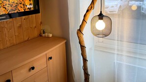 Un mueble de madera con cajones, un televisor montado encima y una lámpara de pie de diseño original con forma de rama y pantalla tejida.