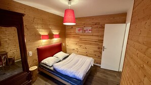 Una habitación con paneles de madera, una cama, una lámpara colgante roja y una puerta blanca.