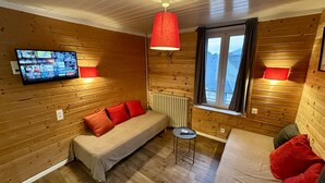 Una habitación de cabaña acogedora con interior de madera, un sofá, una cama, un televisor montado en la pared y un ventanal con cortinas.