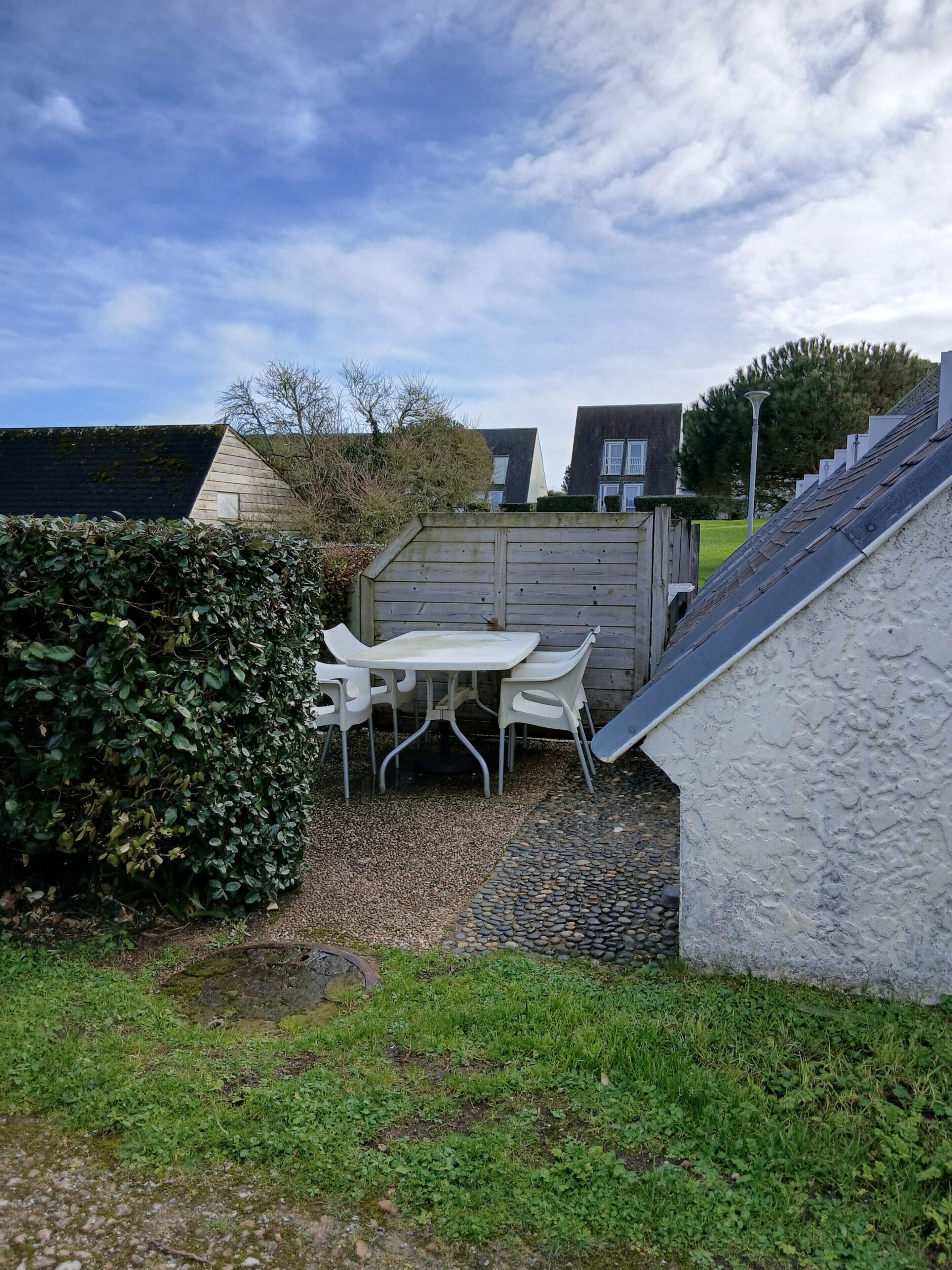A patio area with a table and chairs, surrounded by a wooden fence and a hedge.