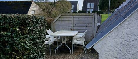 A patio area with a table and chairs, surrounded by a wooden fence and a hedge.