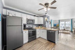 A modern kitchen with white cabinets, stainless steel appliances, and a wooden floor. - Trident by Bayshore | 2BR Apartment (Ocean City)