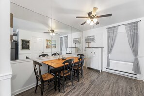 A dining area with a wooden table and chairs, a ceiling fan, and a large mirror. - Trident by Bayshore | 2BR Apartment (Ocean City)