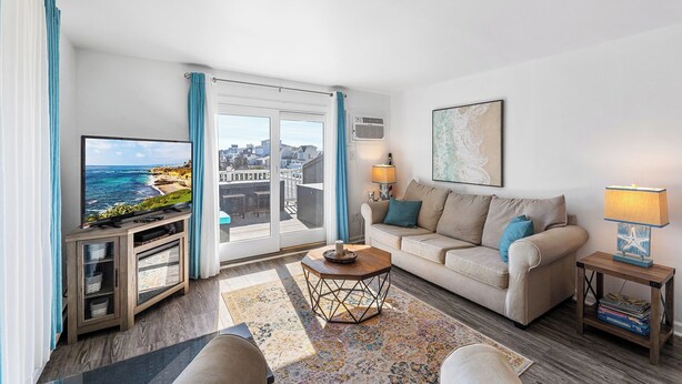Ein Wohnzimmer mit Fernseher, Sofa und Couchtisch, mit Blick auf die Stadt durch große Fenster.