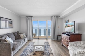En stue med sofa, sofabord, TV-møbel og havudsigt fra en balkon.