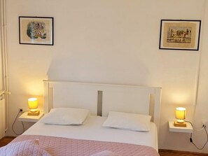 Ein Schlafzimmer mit einem Bett, zwei Nachttischen mit Lampen und zwei gerahmten Bildern an der Wand.