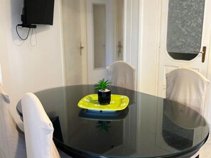 A round glass table with a small potted plant on a yellow plate, surrounded by white chairs in a room with a white door and a window with a textured view. - Apartment Moreno 2 With Seaview (Marina)