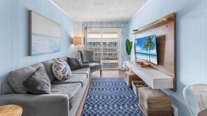 Ein Wohnzimmer mit Sofa, Fernseher und Blick auf den Balkon.