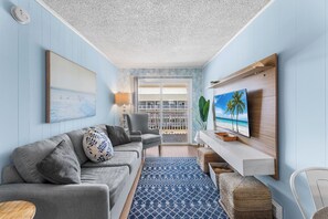 A living room with a sofa, TV, and a view of the balcony. - Atlantic Court 303 Steps to the beach (Ocean City)