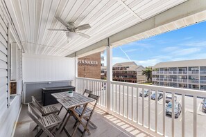 A balcony with a table and chairs, a ceiling fan, and a view of a parking lot and buildings. - Atlantic Court 303 Steps to the beach (Ocean City)