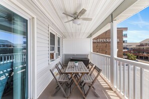 A covered balcony with a table and chairs, a ceiling fan, and a view of a building with a sign. - Atlantic Court 303 Steps to the beach (Ocean City)