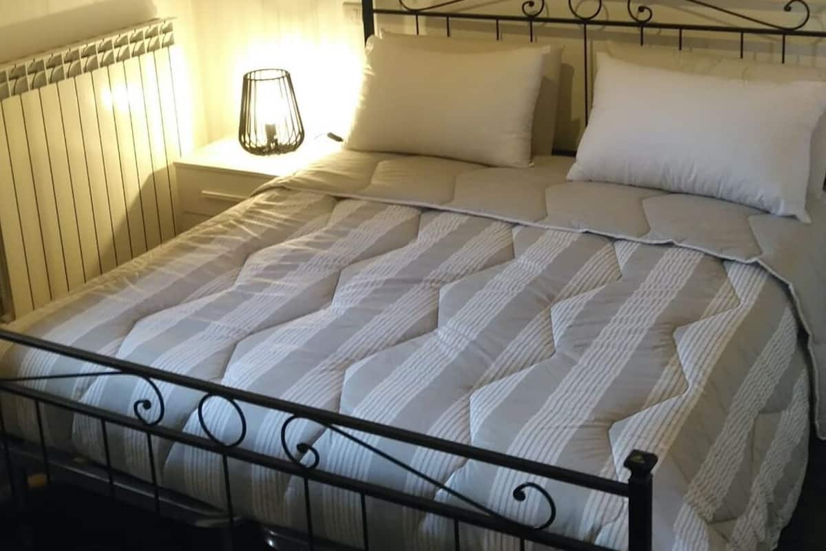 A neatly made bed with a metal frame, a world map on the wall, and a bedside lamp.