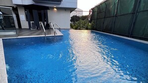 An indoor swimming pool with clear blue water, a metal ladder, and a building with a balcony in the background. - Luxury Studio Apartments in Accra  (Accra)