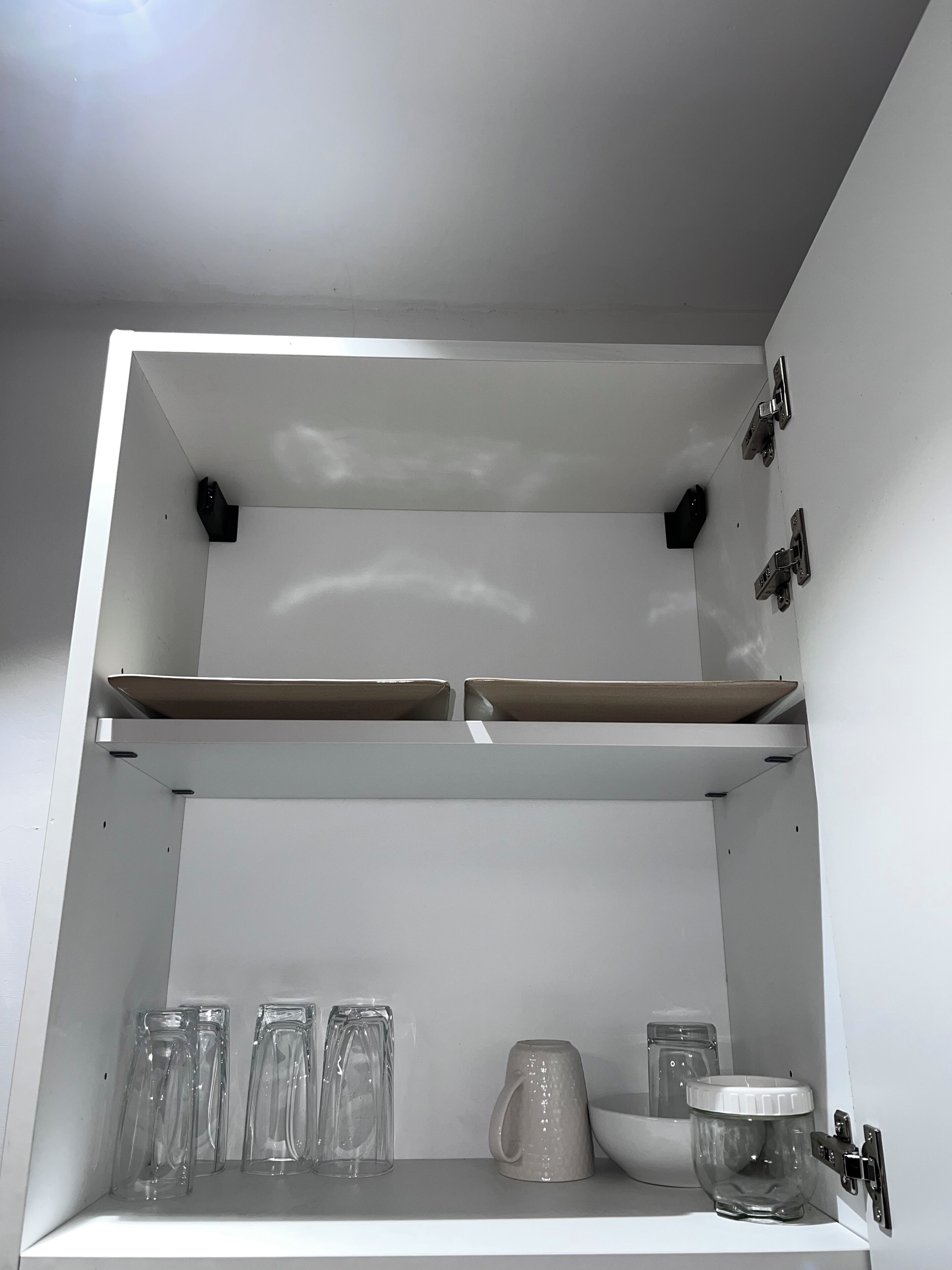 A white shelf unit with two open shelves and a lower shelf holding clear glassware and a ceramic mug.
