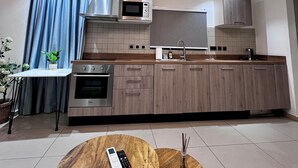 A modern kitchen with built-in appliances, a wooden countertop, and a dining area with two wooden tables. - Luxury Studio Apartments in Accra  (Accra)