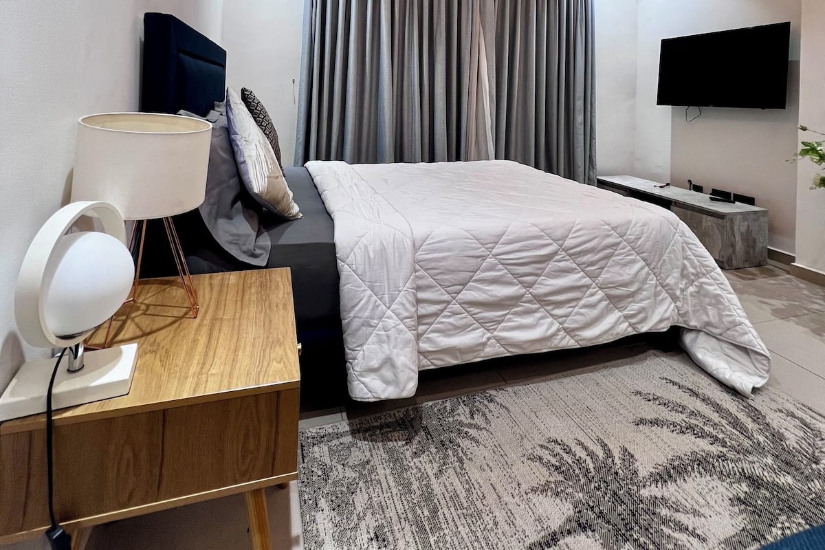 Un dormitorio moderno con cama, mesita de noche, lámpara y televisor de pantalla plana montado en la pared.