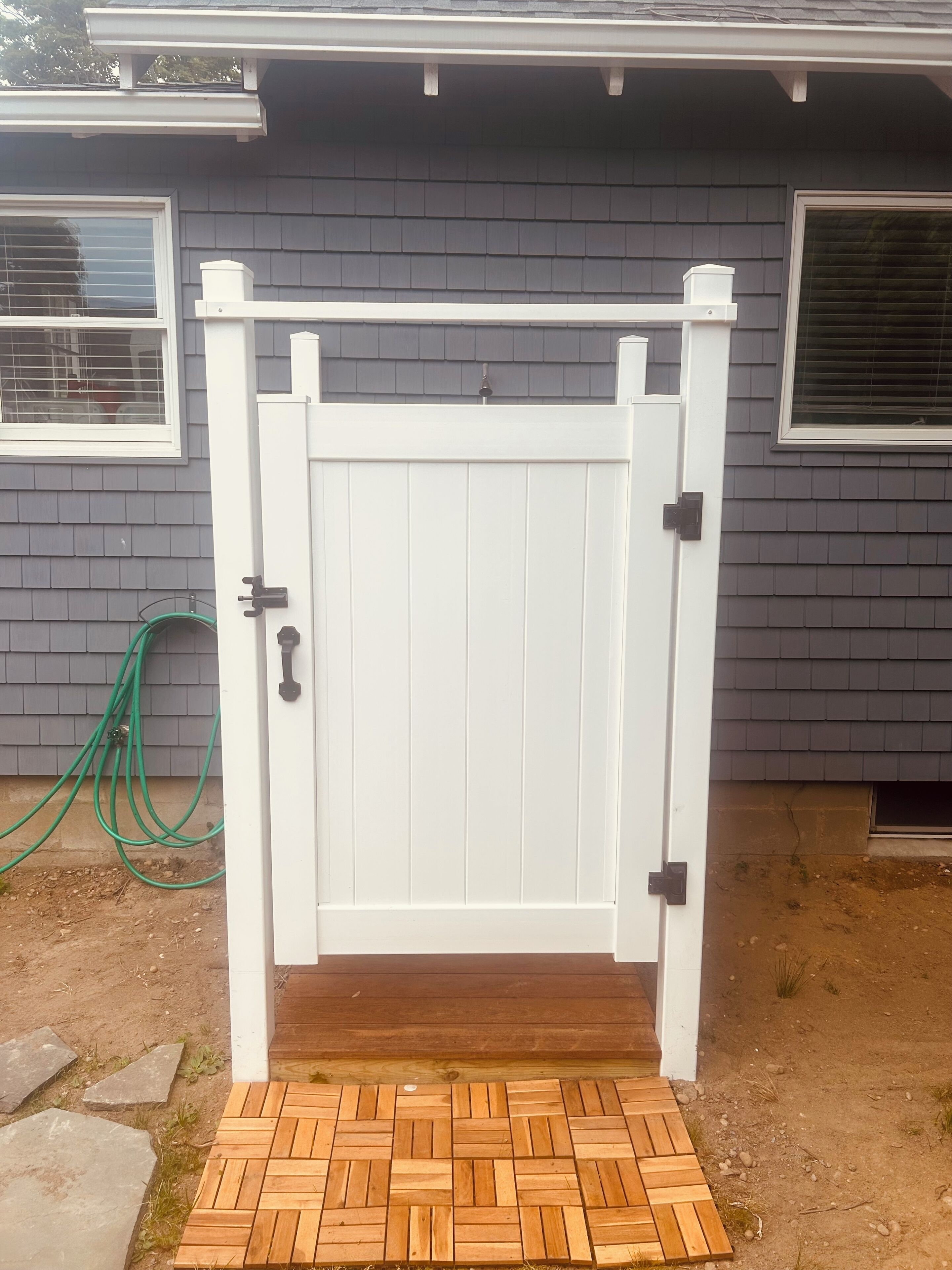 A white gate with a wooden step leading up to a house with grey siding and a window with a white frame.