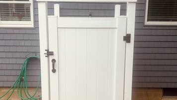 A white gate with a wooden step leading up to a house with grey siding and a window with a white frame.