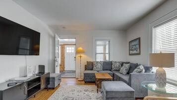 A modern living room with a grey sofa, a glass coffee table, a flat-screen TV, and a lamp.