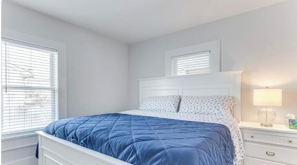 Une chambre à coucher avec un lit, une table de chevet, une lampe et une fenêtre avec des stores.