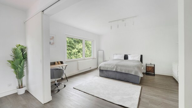 Un dormitorio moderno con cama, escritorio y un ventanal grande.