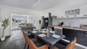 Una cocina moderna con armarios blancos, un comedor con mesa dispuesta para cuatro personas y vista al salón.