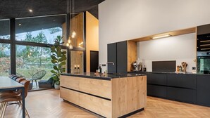 Una cocina moderna con una isla de madera, armarios negros y un ventanal con vistas a árboles.