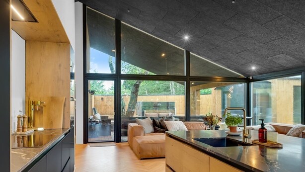 Una cocina moderna con una isla grande, puertas correderas de vidrio a un patio y un rincón de estar acogedor con un sofá y cojines.