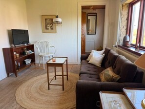 A living room with a sofa, a small table, a television on a stand, a chair, and a decorative hanging light. - 4 Star Holiday Home in Borrby (Borrby)