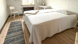 Un dormitorio con una cama grande, una silla, una mesita y una ventana.