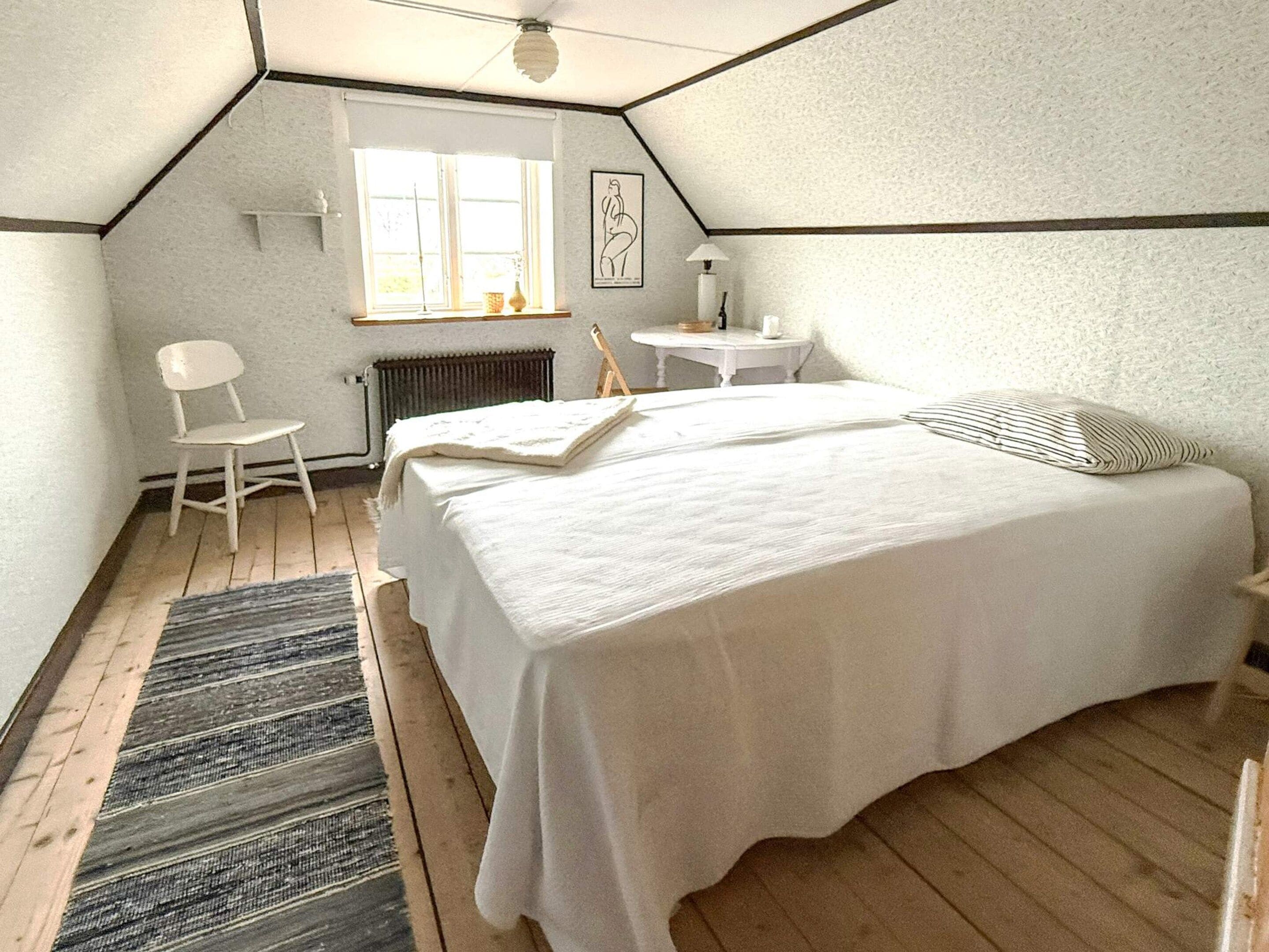 Quarto com cama grande, uma cadeira, uma mesinha e um radiador.