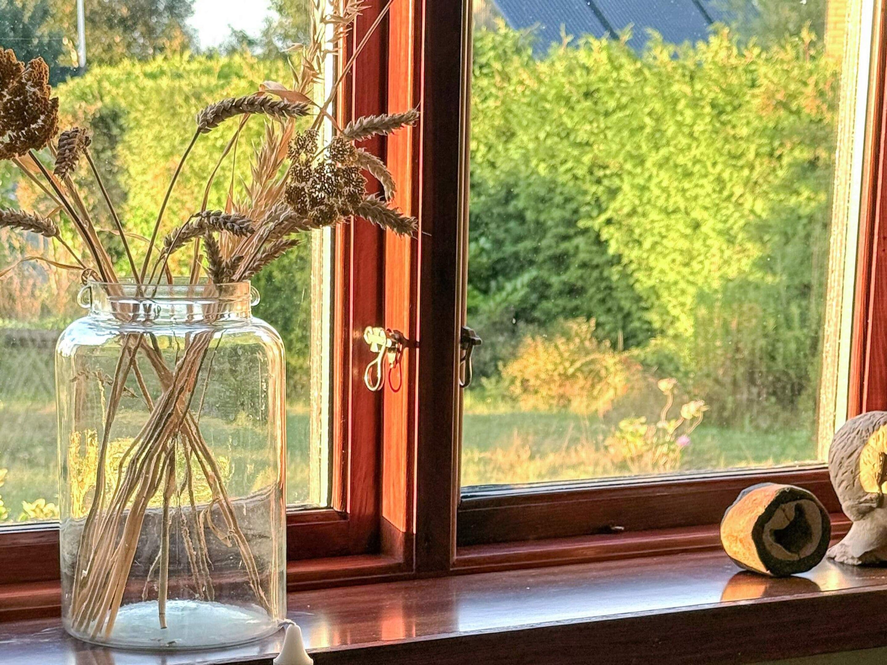 Un jarrón de vidrio transparente con plantas secas sobre un alféizar.
