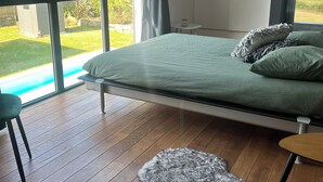 A bedroom with a large bed, a view of a swimming pool, and a wooden floor. - Near La Baule/Historical center.  Villa located in a bubble of Serenity. (Guérande)