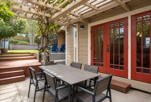 An outdoor patio with a wooden table and chairs, a red door, and a pergola structure. - Spa + BBQ + Big Backyard | Walk to Downtown Paso | Backyard Vines on Olive (Paso Robles)