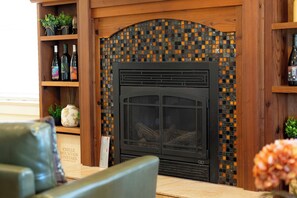 A fireplace with a mosaic tile surround, a wooden shelf with wine bottles, and a chair in the foreground. - Spa + BBQ + Big Backyard | Walk to Downtown Paso | Backyard Vines on Olive (Paso Robles)