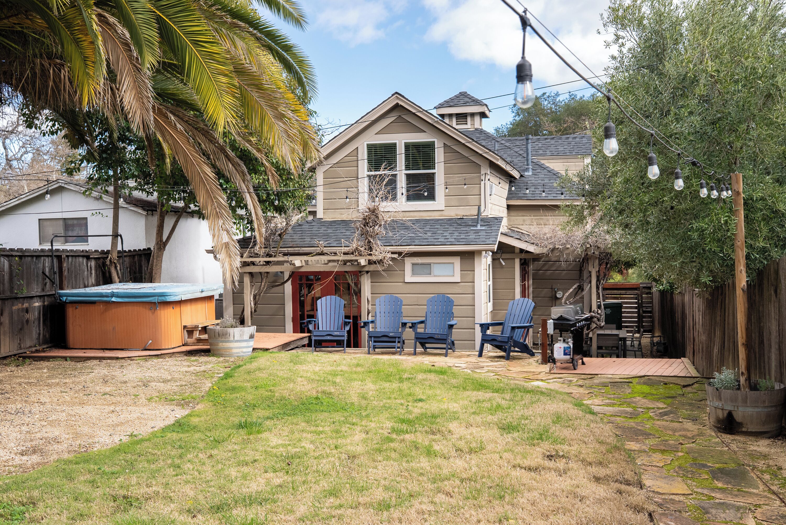 A backyard with a hot tub, patio chairs, and a wooden deck.