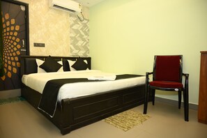 A bedroom with a bed, a chair, and a wall-mounted air conditioner. - Raju Inn (Puri)