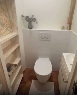 A small bathroom with a toilet, a sink, and a shelf with books. - Modern 1bdr apt Near Moulin Rouge / Montmartre (Paris)
