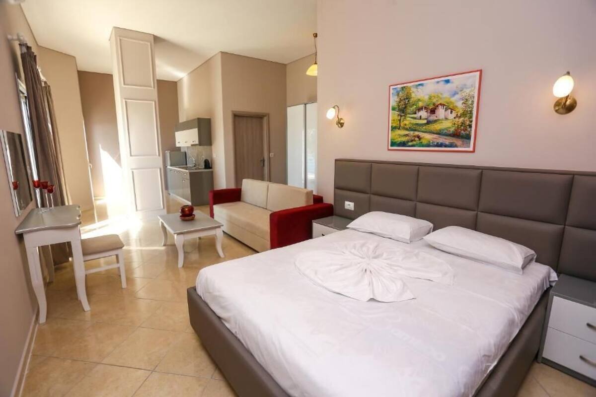 A hotel room with a bed, a desk, a chair, a sofa, and a painting on the wall.