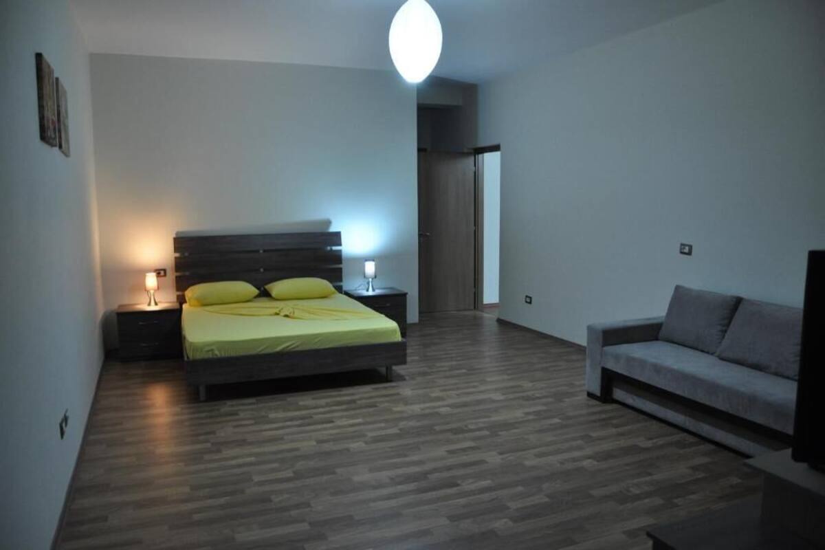 A bedroom with a bed, bedside tables, a lamp, a sofa, and a TV.