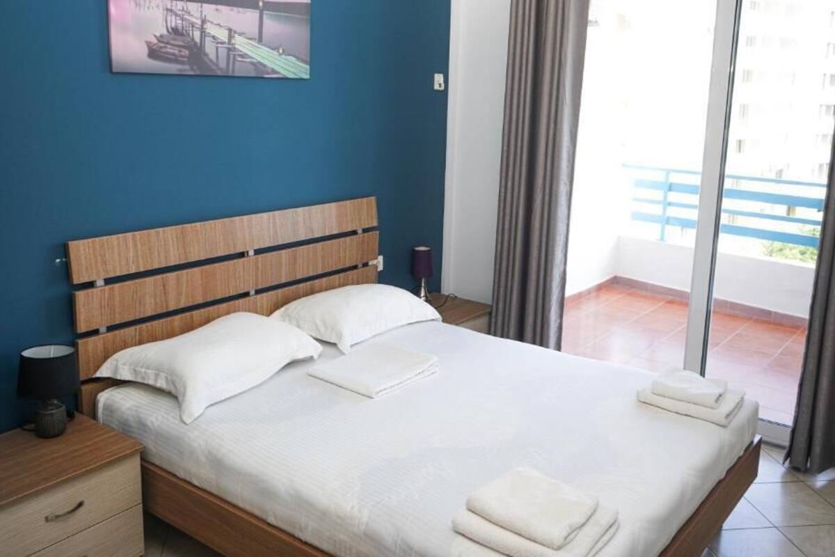 A bedroom with a wooden headboard, a bed with white linens, a nightstand with a lamp, and a view of a balcony through a sliding door.