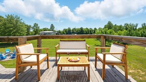 Un terrazzo in legno con un divano, due poltrone e un tavolo con un piatto di cibo e due bicchieri di vino.
