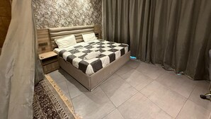 A bedroom with a large bed, a nightstand, a patterned wall, and a ceiling fan. - spira.staycation (Noida)